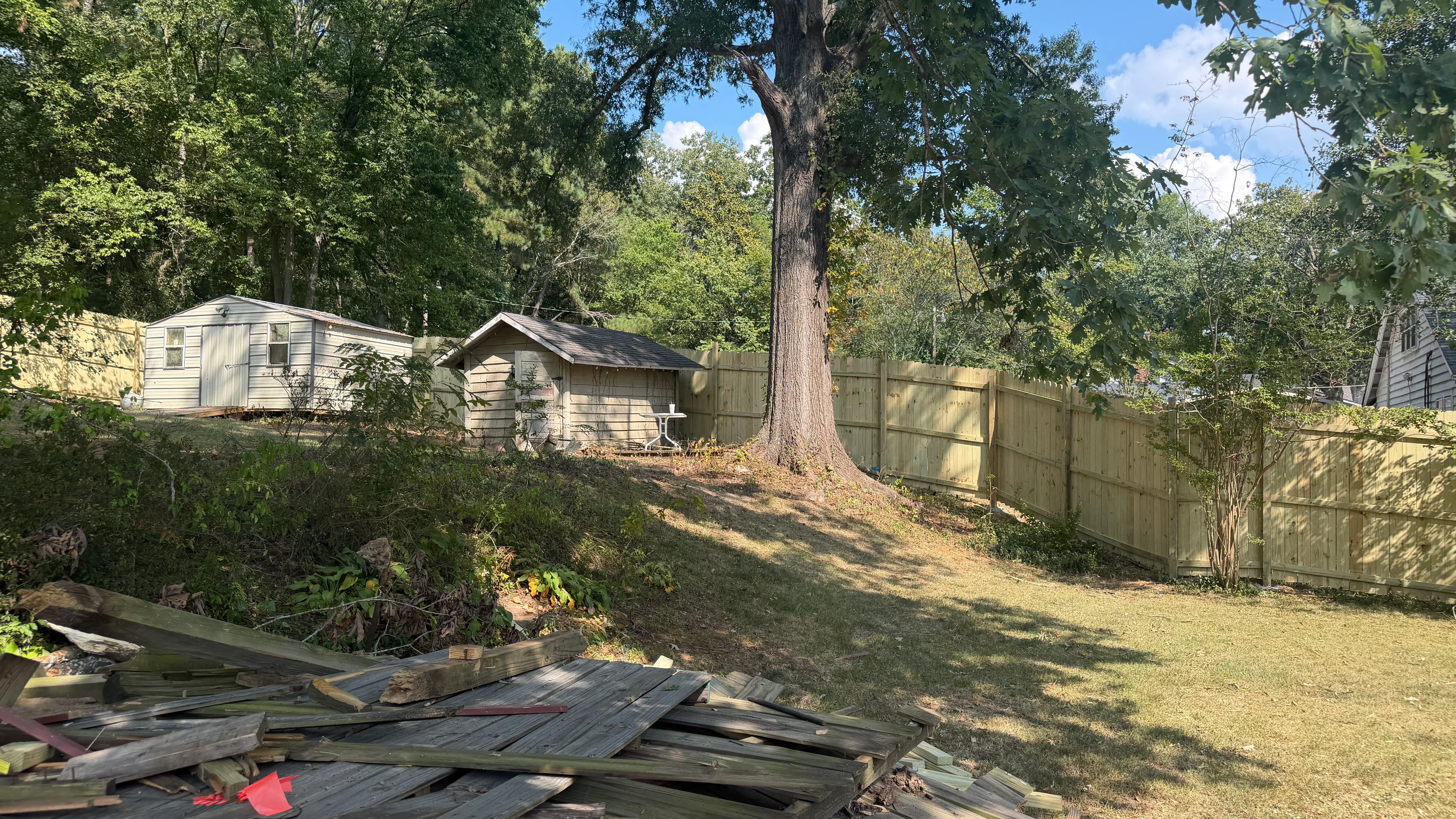 Wooden privacy fence installation on sloped yard with mature trees and graded landscape