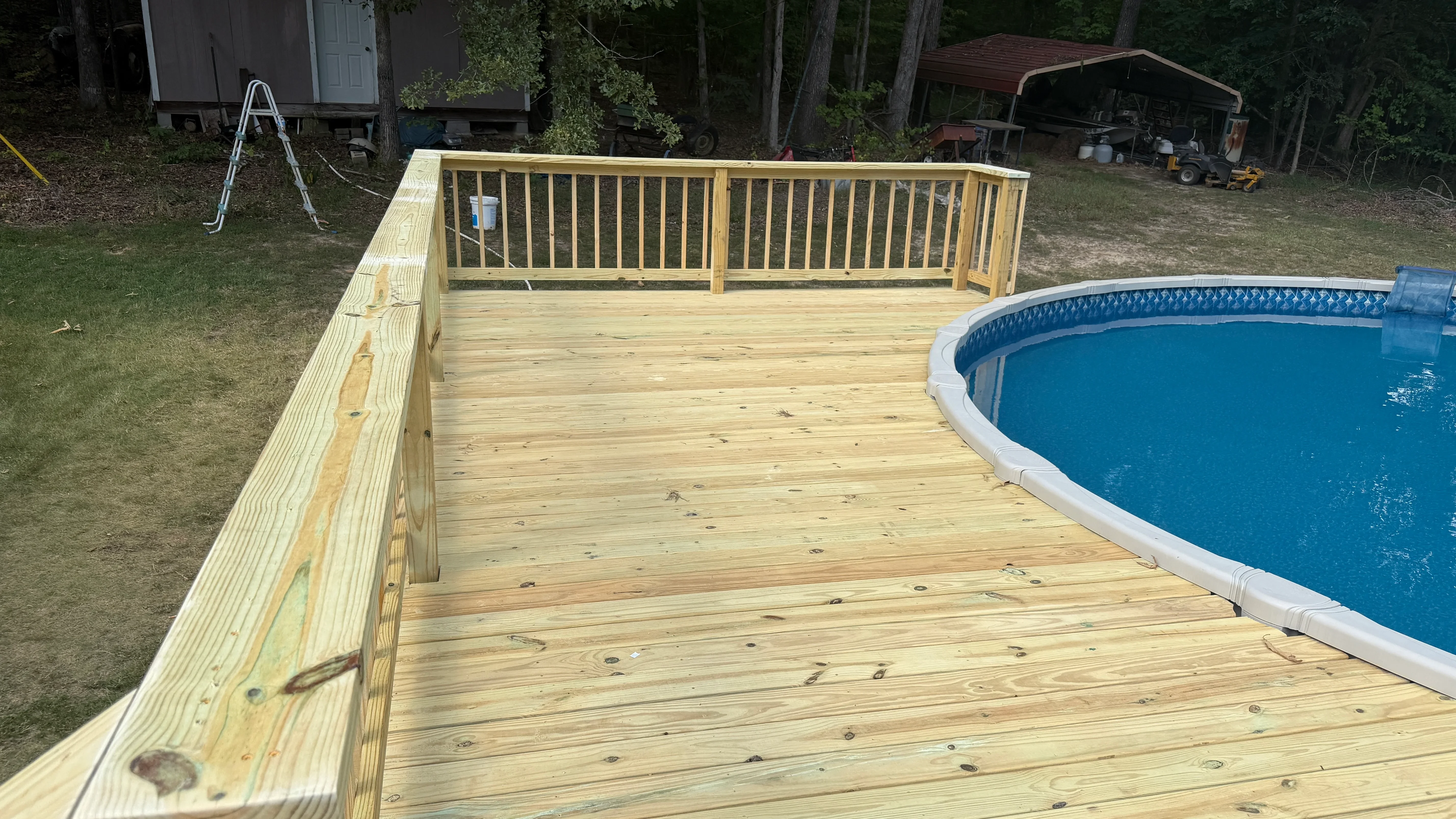 Pressure-treated wood deck with vertical spindle railings next to in-ground pool
