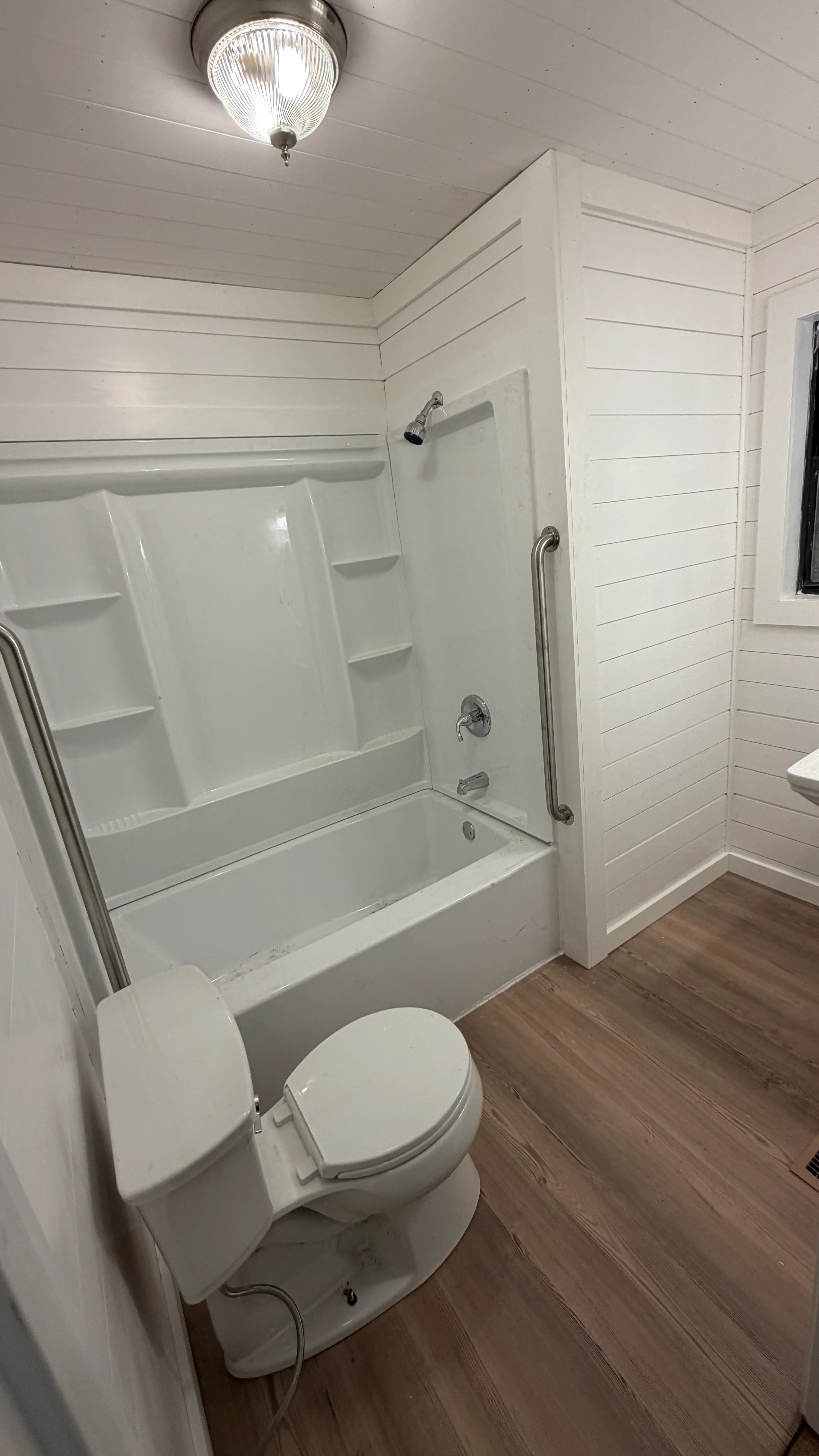 White bathroom with shiplap walls, fiberglass shower surround, chrome grab bars, and vinyl plank flooring