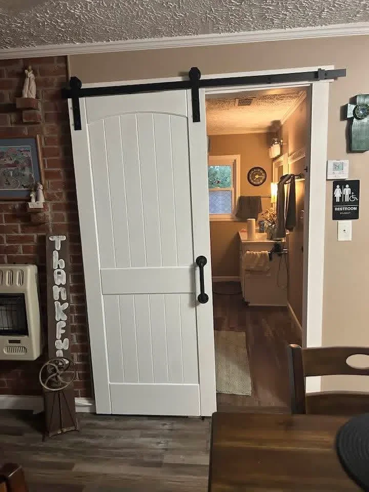 White vertical-paneled sliding barn door with black hardware and track system installed as interior room divider