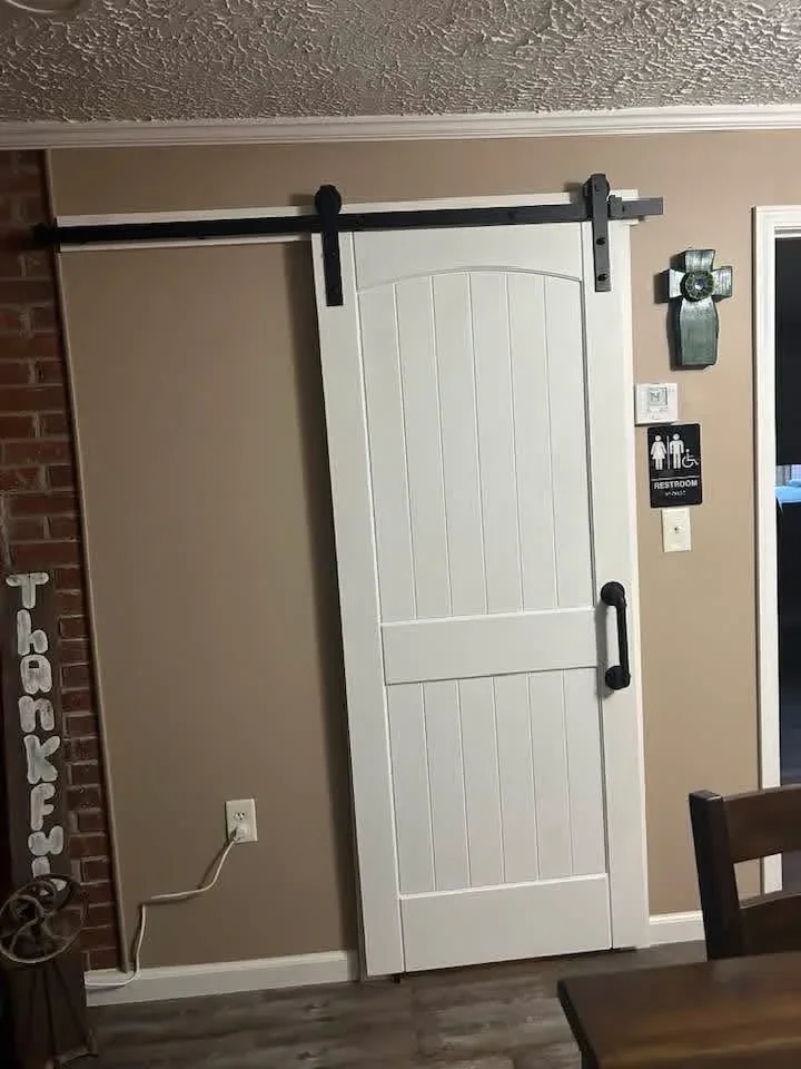 White vertical panel barn door on black sliding track with black hardware handles