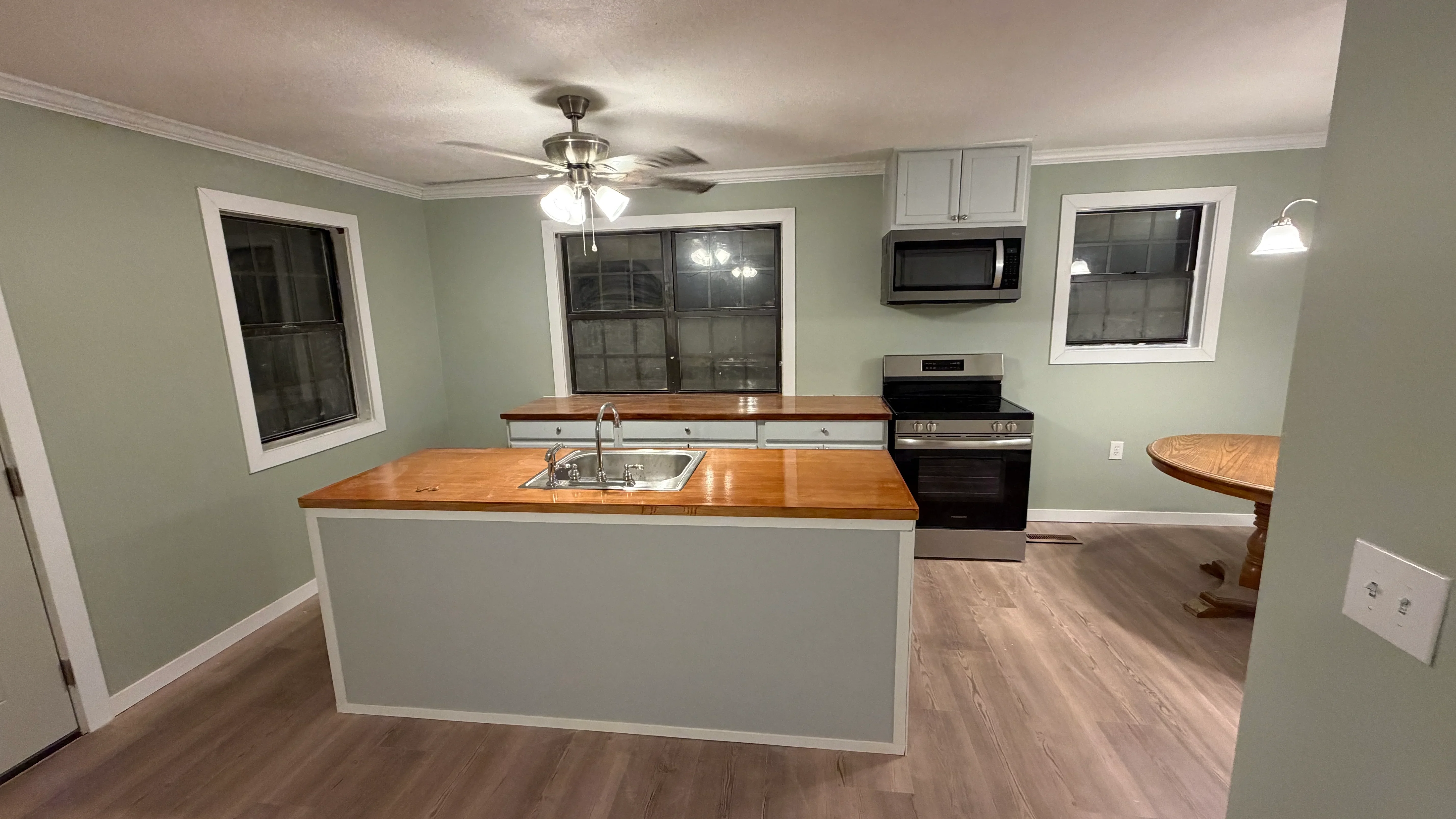 Kitchen with white island, wood countertops, stainless steel appliances, sage green walls, hardwood flooring