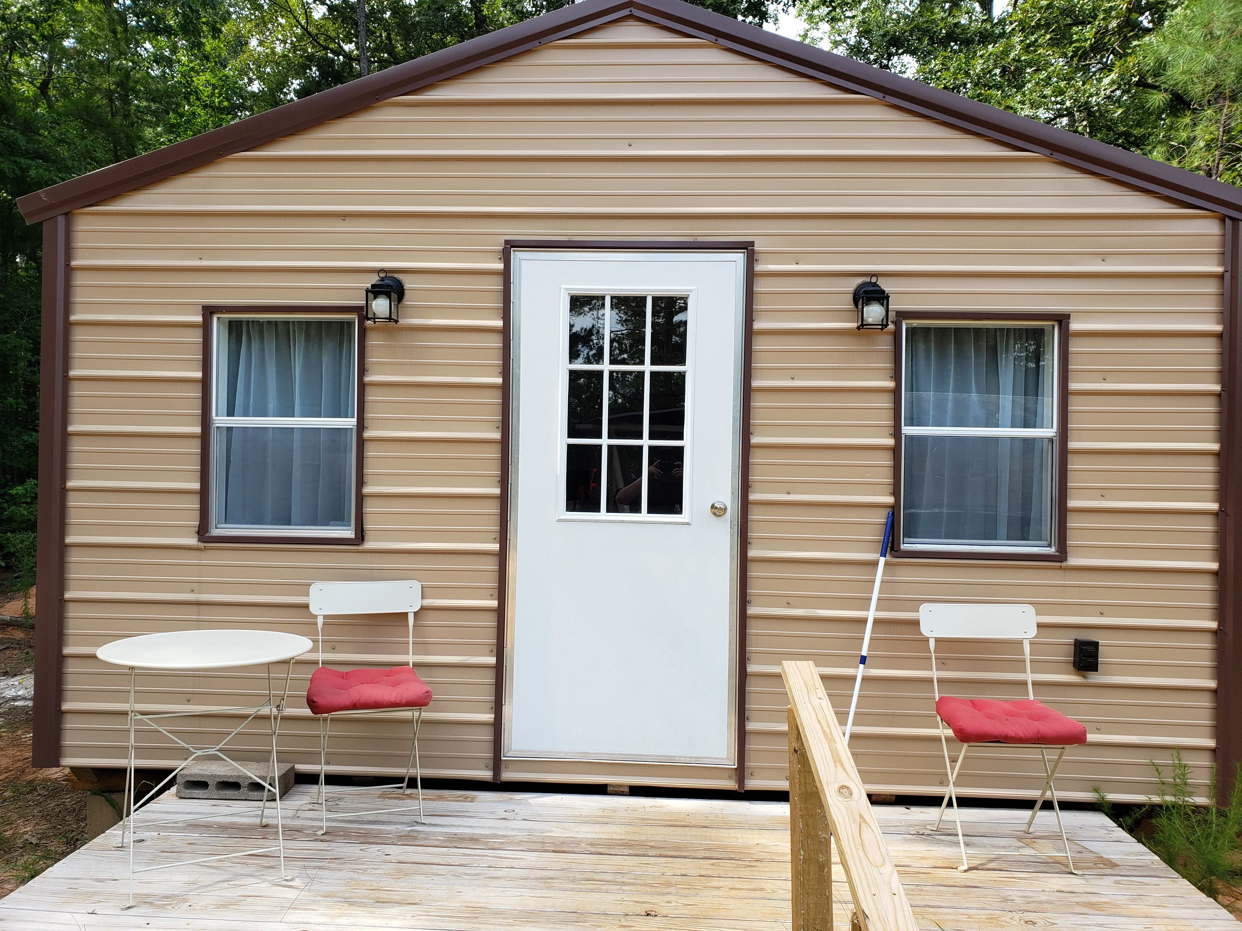 Tan vinyl siding shed with brown trim, double-hung windows, white entry door, and wood deck