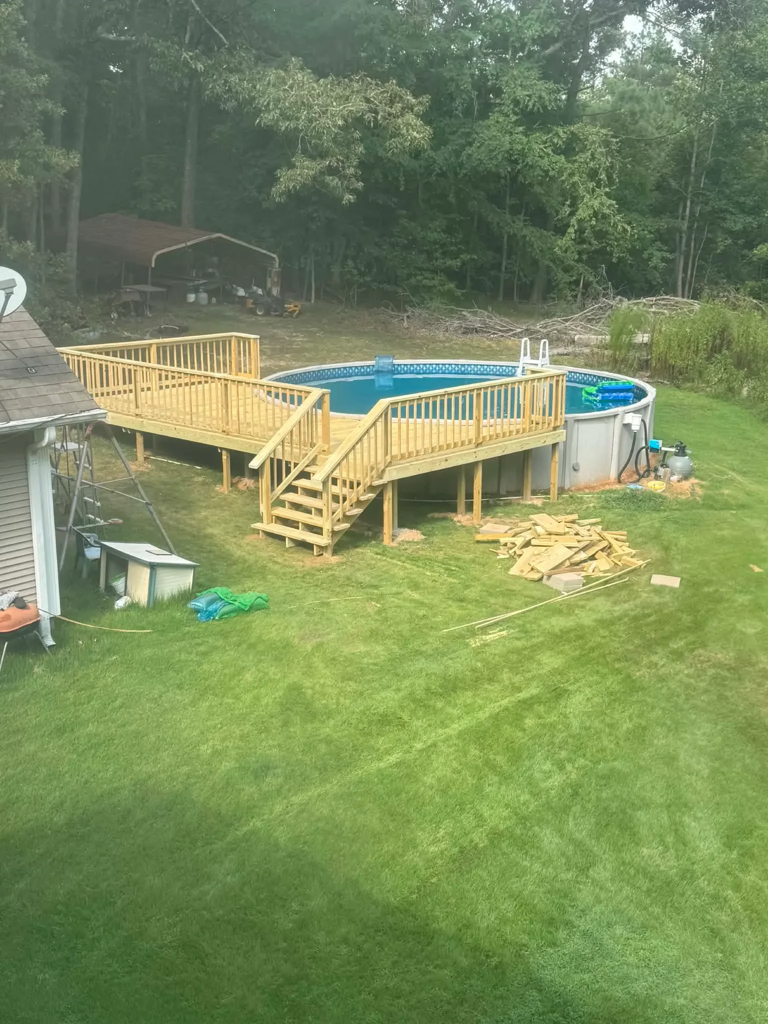 Pressure-treated wood deck with railings surrounding above-ground pool with stairs