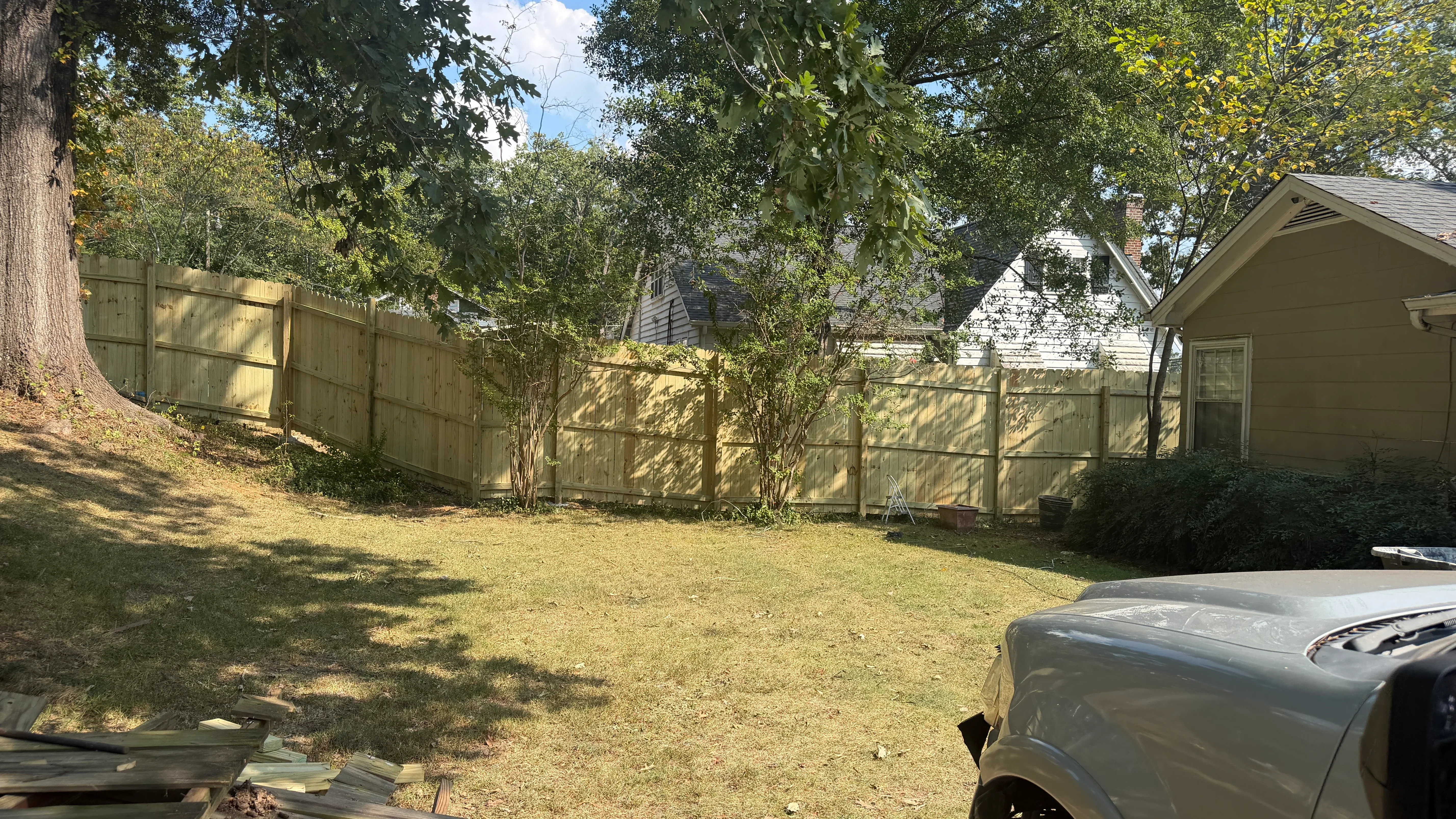 Wooden privacy fence with vertical boards installed in residential backyard with mature trees