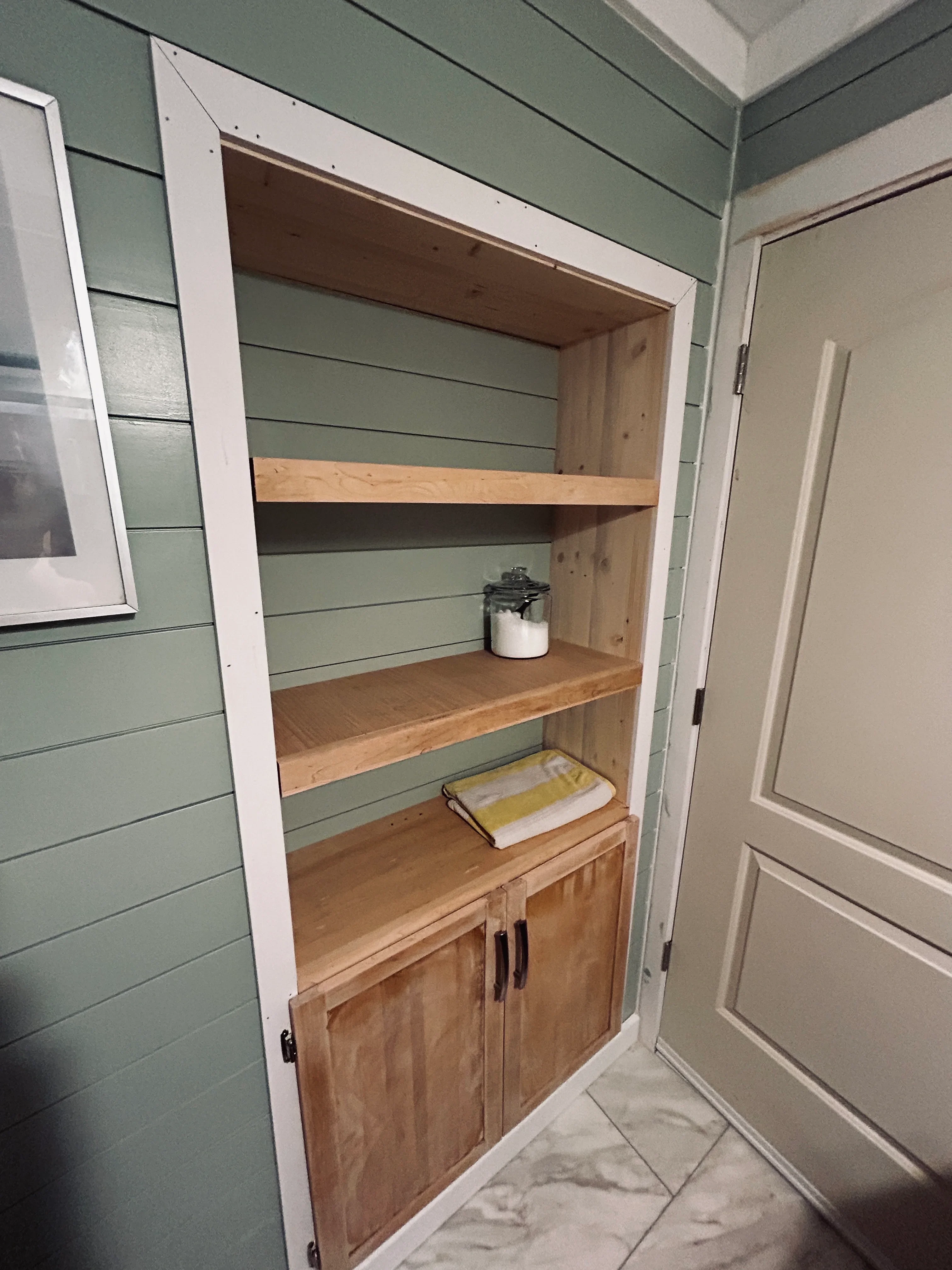 Custom built-in shelving with wood shelves, white trim, and lower cabinet storage against shiplap wall
