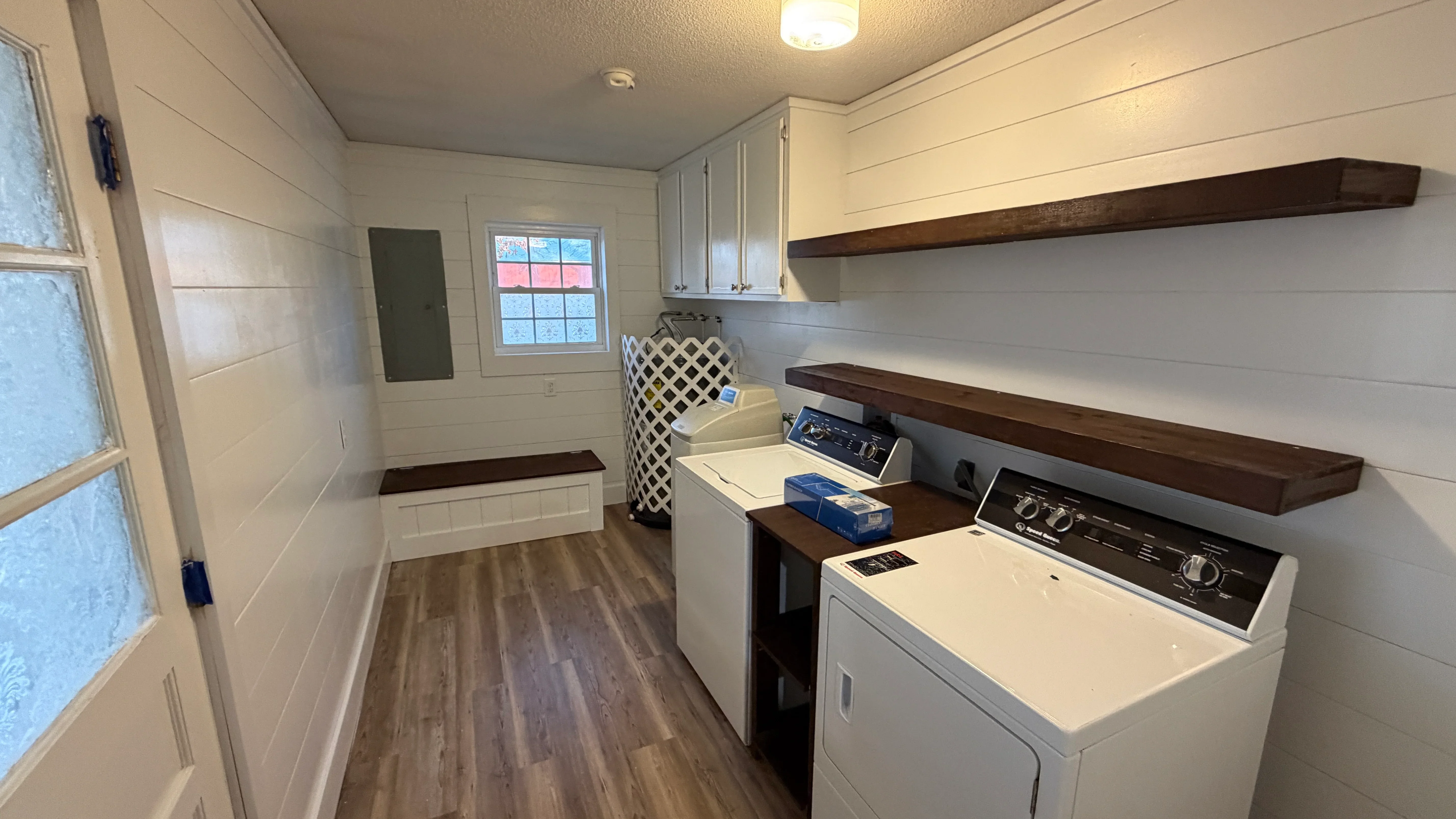 White shiplap laundry room with dark wood shelves, white cabinets, and modern washer/dryer setup