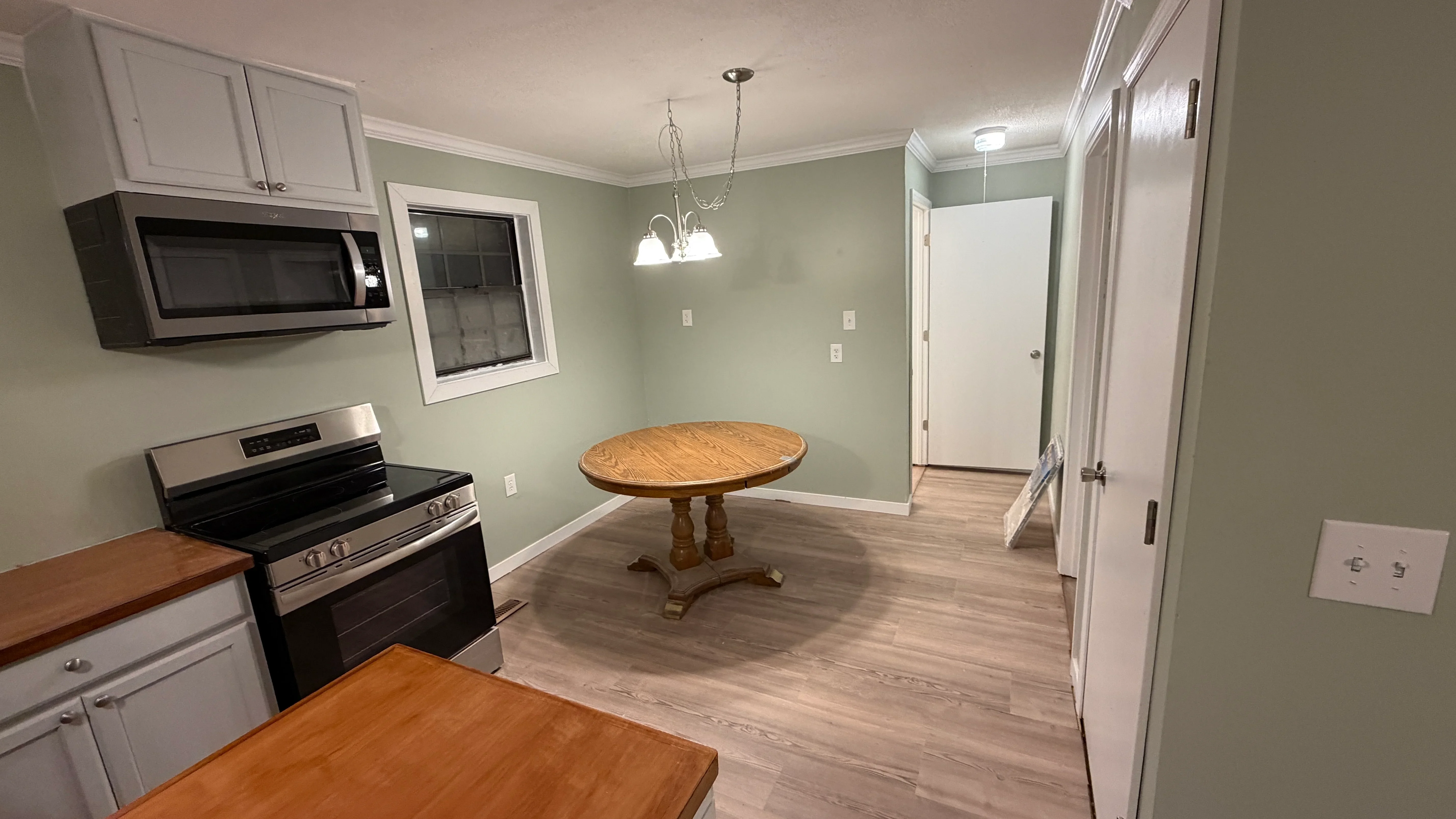 Kitchen with white cabinets, stainless steel range, and dining area with vinyl plank flooring and sage green walls