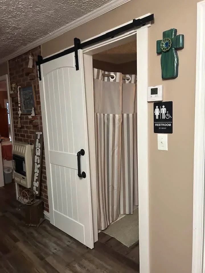 White vertical-panel sliding barn door with black hardware in commercial restroom