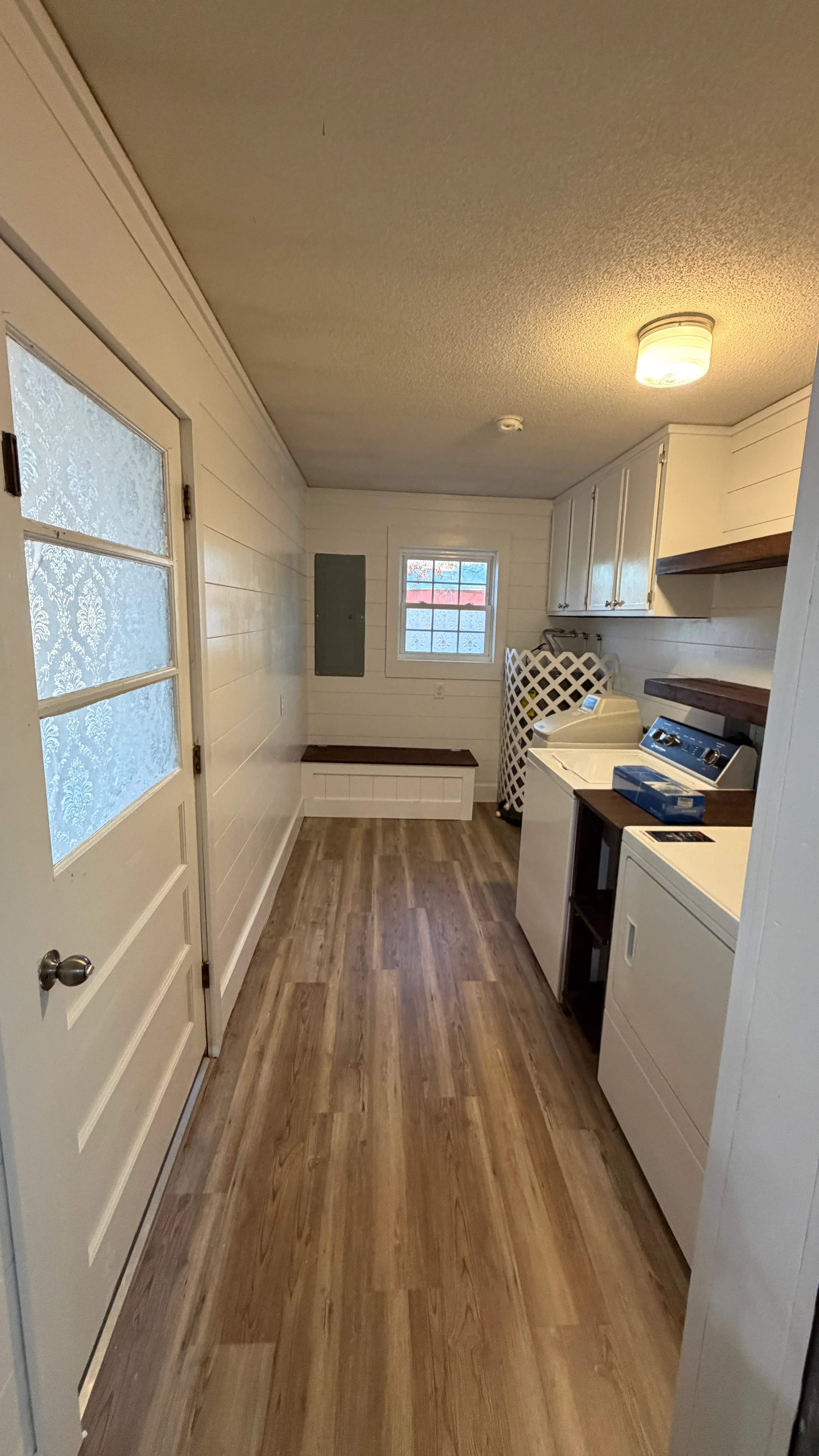 Galley kitchen with white cabinets, wood-tone vinyl flooring, and shiplap walls