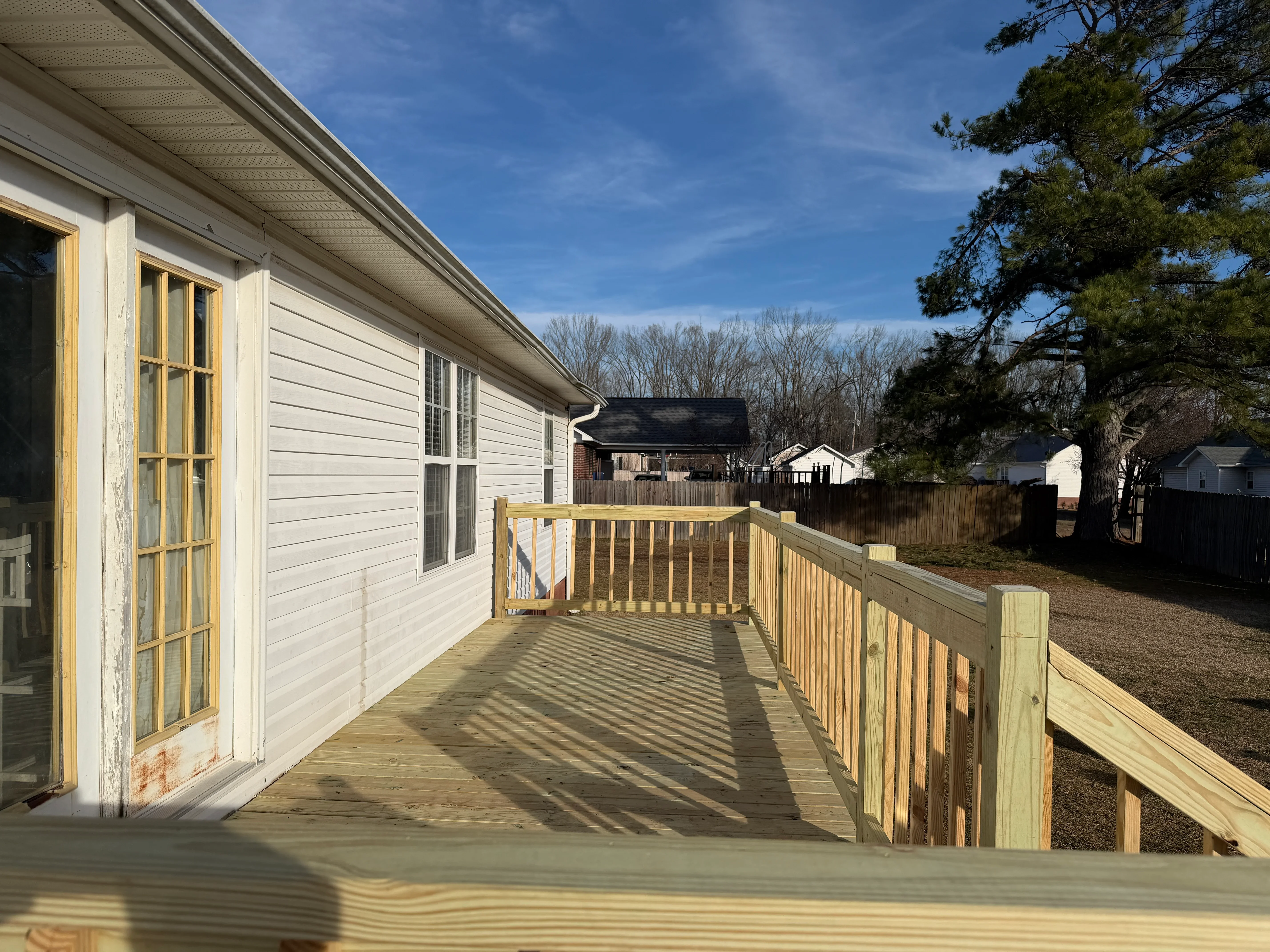 Newly built wooden deck with railings attached to white mobile home exterior