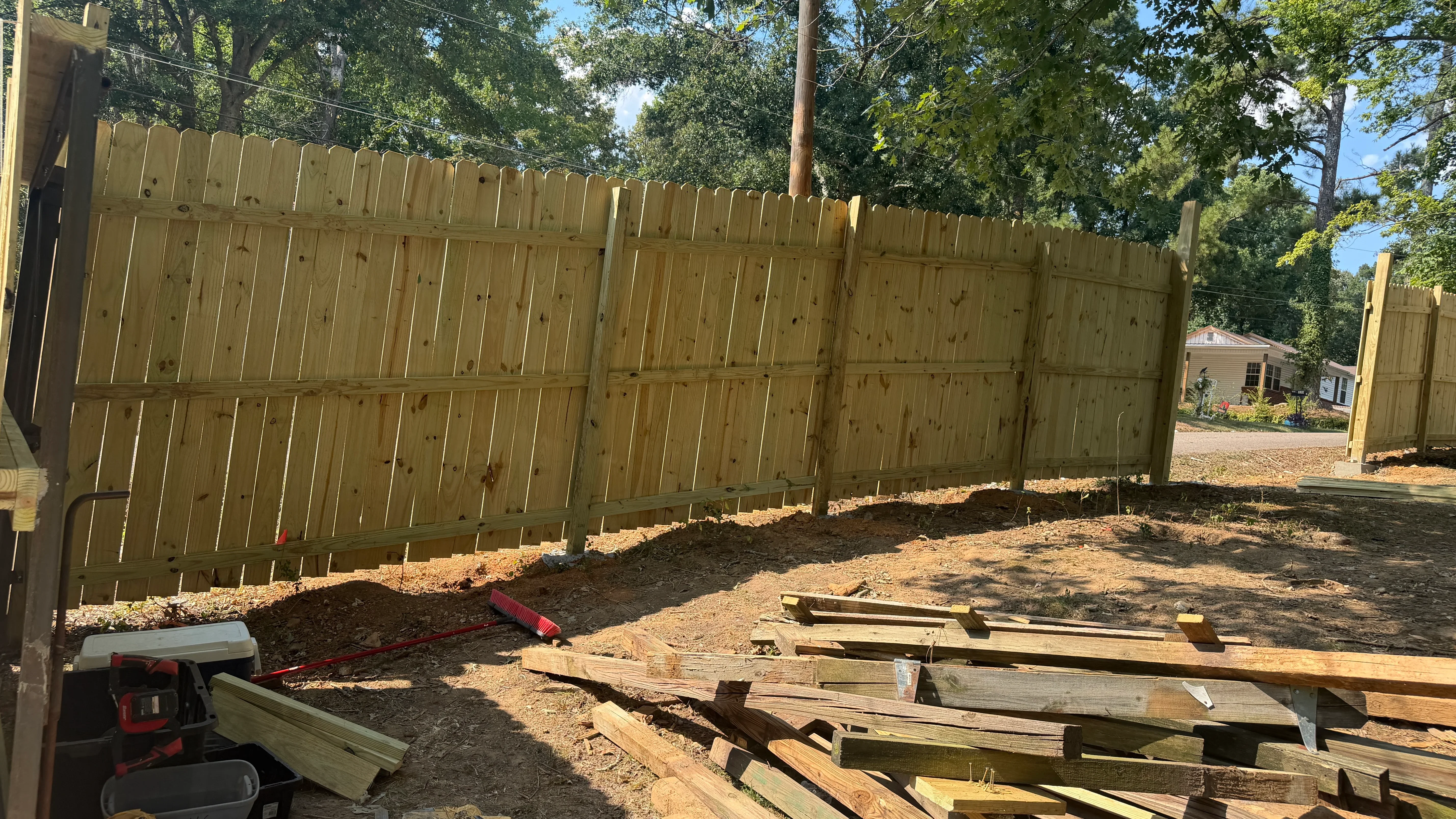 Newly installed pressure-treated wood privacy fence with scalloped top and vertical boards