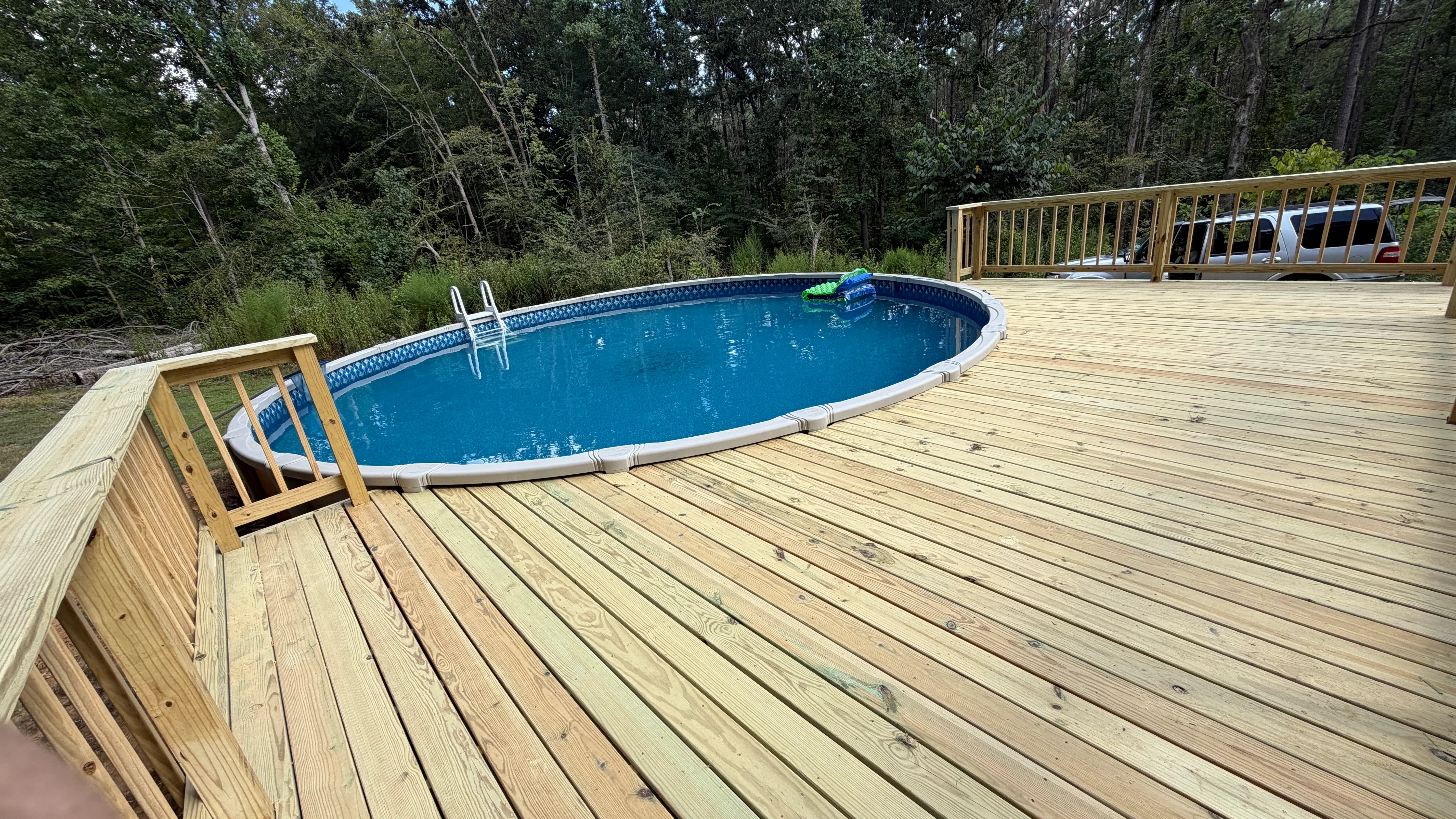 Pressure-treated wood deck with pool stairs and railings surrounding blue above-ground pool