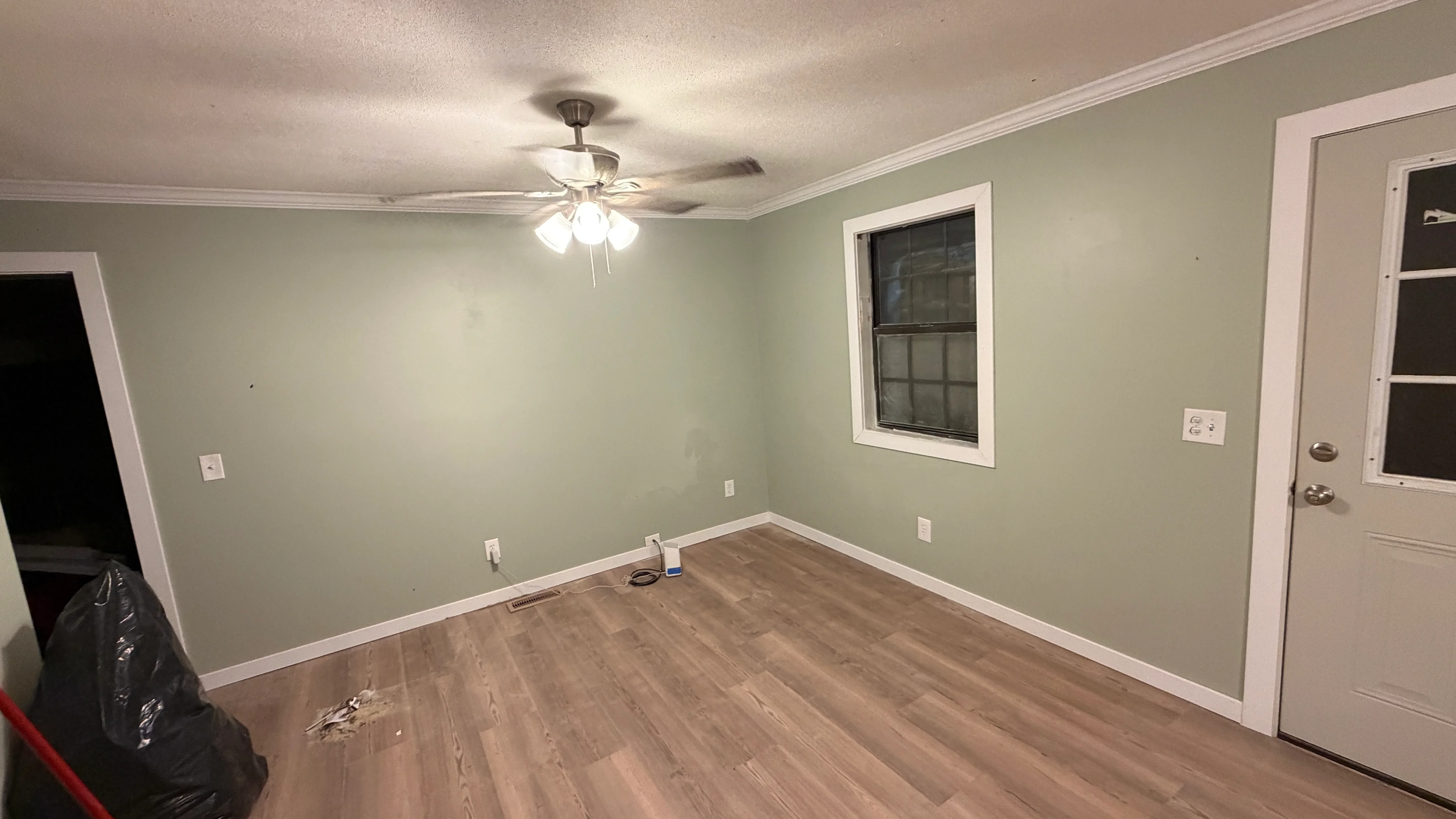 Renovated room with sage green walls, white trim, laminate wood flooring, and ceiling fan